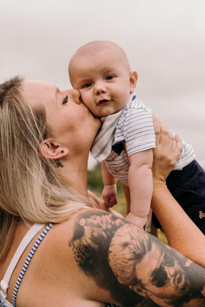 Mum is kissing her baby boy on his cheek. He is looking at the camera. Lovely family connection. Family photographer in Hampshire. Ewa Jones Photography