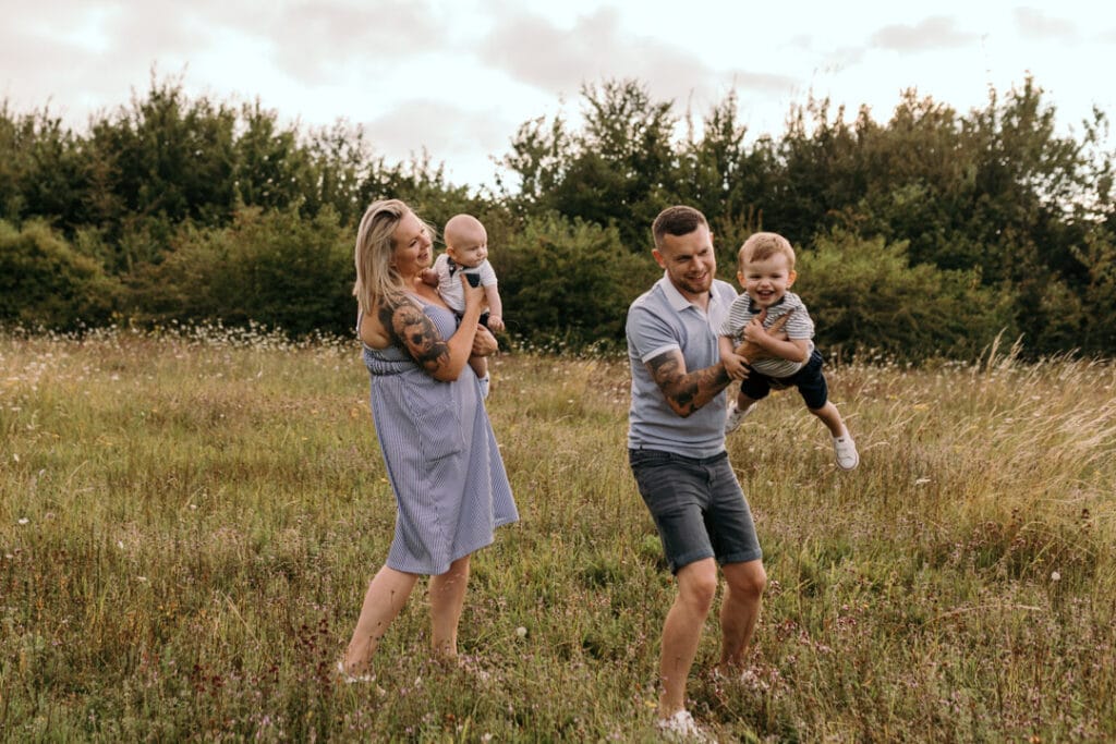 Family of four is dancing in the field of flowers. Unposed family photo session in Basingstoke. Family photographer in Hampshire. Ewa Jones Photography