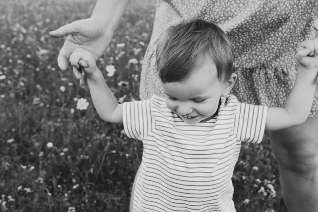 mum is holding her little boy and his is walking in the field of summer flowers. Black and white image. Basingstoke photographer. Ewa Jones Photography