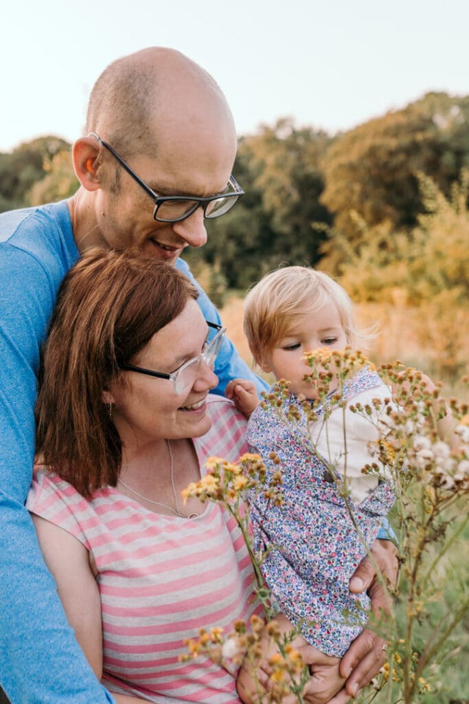family of three is cuddling close to each other and looking at their daughter who is looking at the late summer flowers. Family photo shoot in Hampshire. Ewa Jones Photography