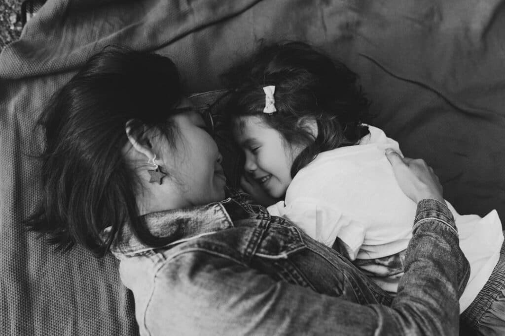 Mum and daughter are laying on the blanket and cuddling to each other. Lovely black and white candid image of mum and daughter. Basingstoke photographer. Ewa Jones Photography