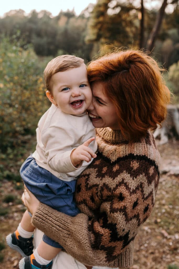 Mum is holding her little baby boy in her arms and she is close to him. He is looking at the camera and smiling. My favourite family photographs of 2021. Ewa Jones Photography