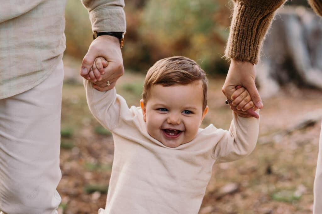 lIttle boy is smiling to the camera and mum and dad are holding his hands. My favourite family photographs of 2021. Hampshire photographer. Ewa Jones Photography