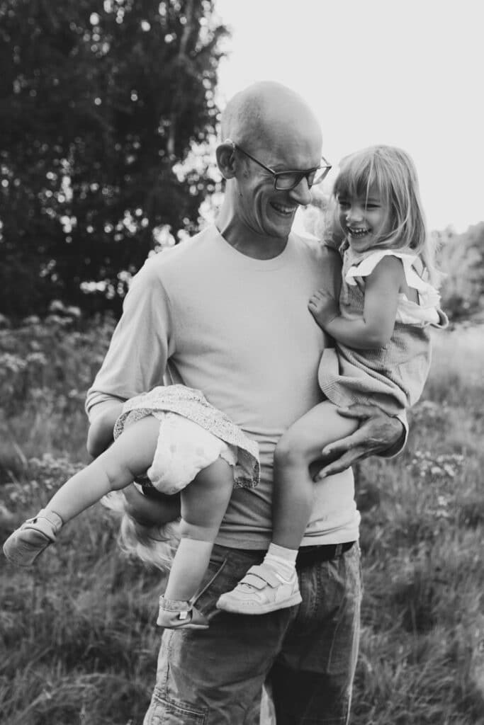 Dad is holding his two girls in his arms. one is flipped upside down and they are all laughing. My favourite family photographs of 2021. family photographer in Hampshire. Ewa Jones Photography