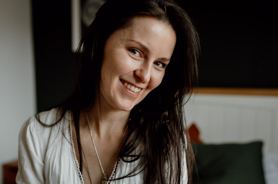 Woman sitting on the bed and looking at the camera. she is wearing a white dress and has her hair down. Goodbye to 2021 and hello to 2022. Basingstoke photographer. Ewa Jones Photography