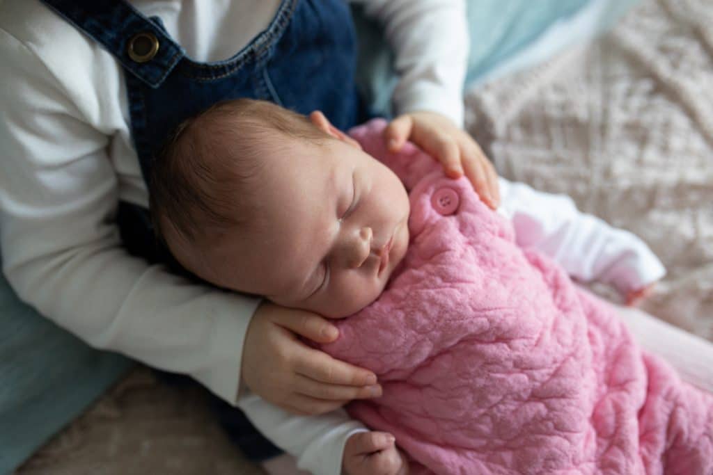 Big sister is holding her newborn baby sister who is sleeping. Natural in home lifestyle newborn photography in Hampshire. Ewa Jones Photography