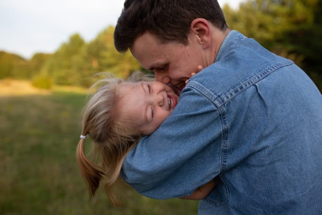 Dad is tickling and kissing her baby daughter and she is laughing. Natural unposed family photo shoot in Basingstoke, Hampshire. Basingstoke photographer. Ewa Jones Photography