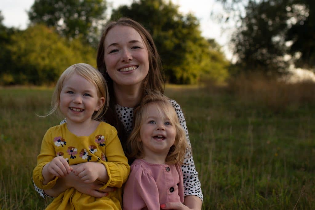 Mum and daughters are sitting in the field of wild grass and smiling. family photo session in Basingstoke, Hampshire. Hampshire photographer. Ewa Jones Photography