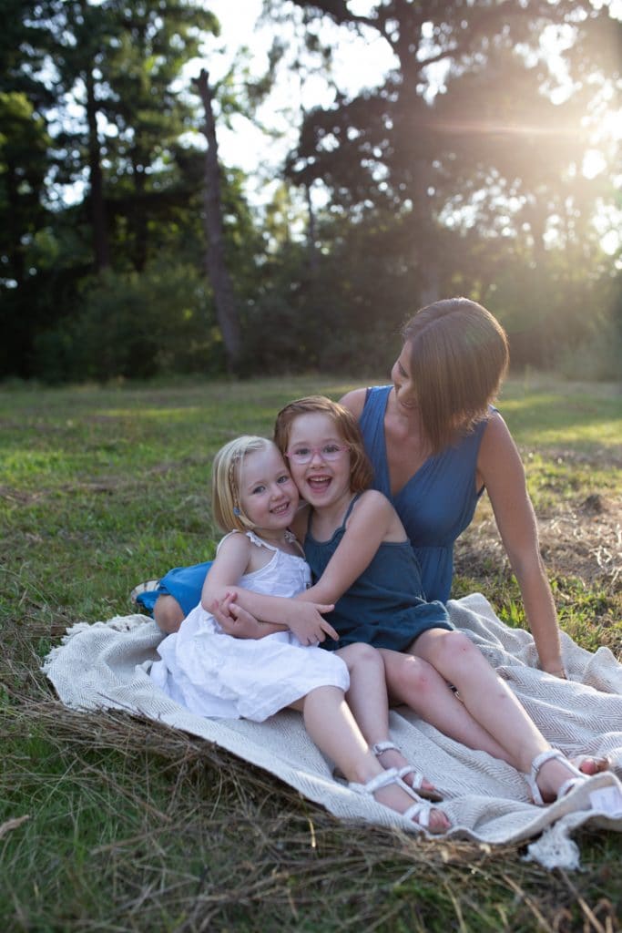 Mum and daughters are sitting in the field of wild grass and smiling. family photo session in Basingstoke, Hampshire. Hampshire photographer. Ewa Jones Photography