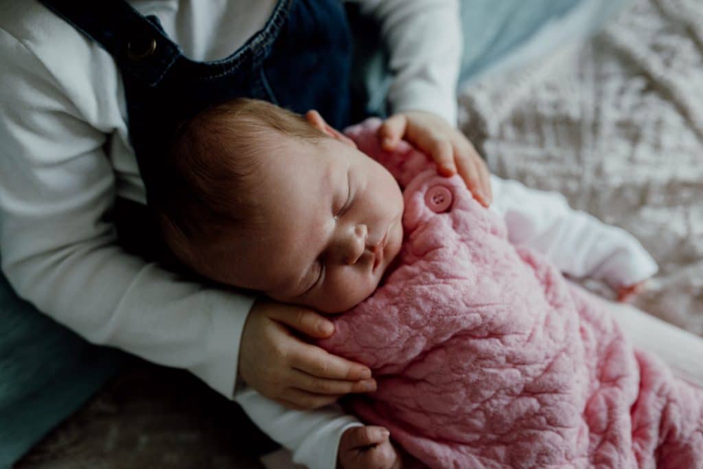 Big sister is holding her newborn baby sister who is sleeping. Natural in home lifestyle newborn photography in Hampshire. Ewa Jones Photography