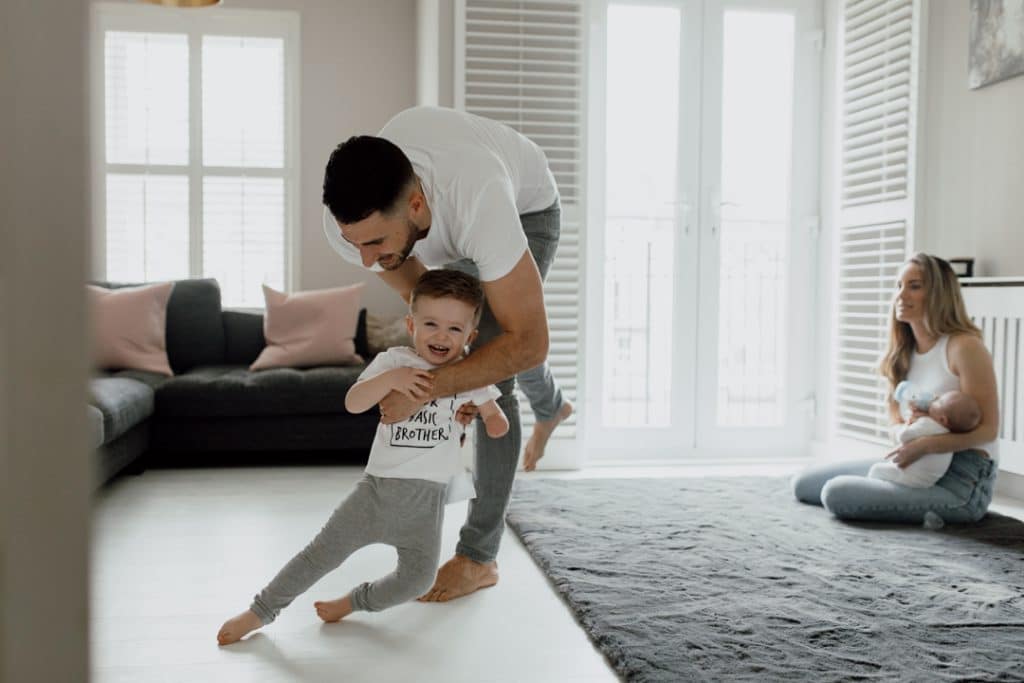 Dad is tickling his son and mum is sitting in the background with a little newborn baby boy. Newborn photographer in Hampshire. Ewa Jones Photography