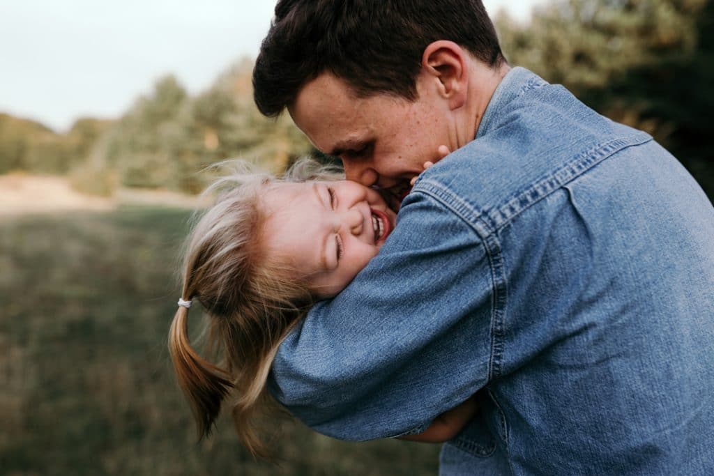 Dad is tickling and kissing her baby daughter and she is laughing. Natural unposed family photo shoot in Basingstoke, Hampshire. Basingstoke photographer. Ewa Jones Photography