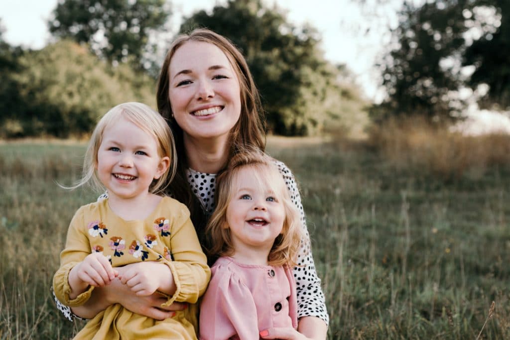 Mum and daughters are sitting in the field of wild grass and smiling. family photo session in Basingstoke, Hampshire. Hampshire photographer. Ewa Jones Photography