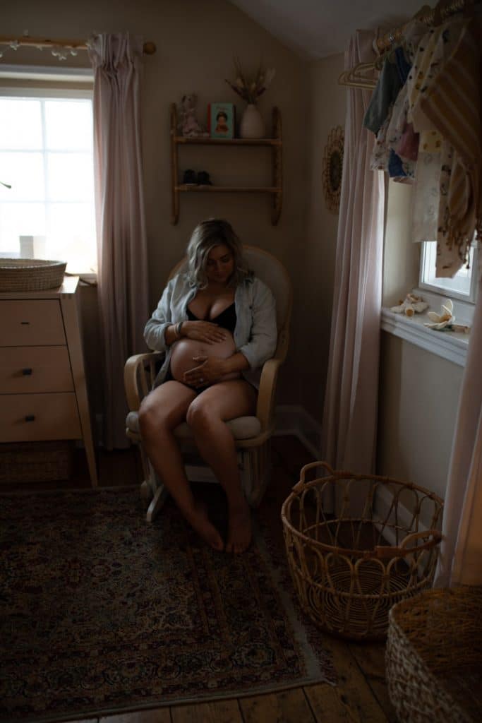 Mum is sitting on the nursing chair and looking down at baby bump. Maternity photo shoot in Hampshire. Hampshire photographer. Ewa Jones Photography