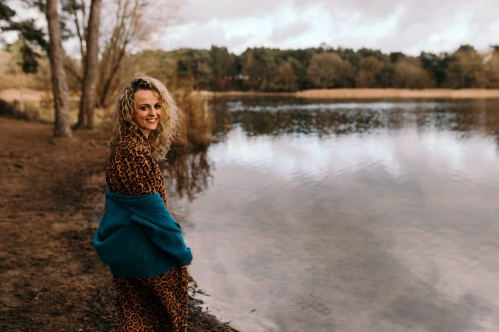 Female is wearing lovely black and brown dress and a blue cardigan. she is smiling the the camera and she is standing next to the water. Female photo shoot in Hampshire. Ewa Jones Photography
