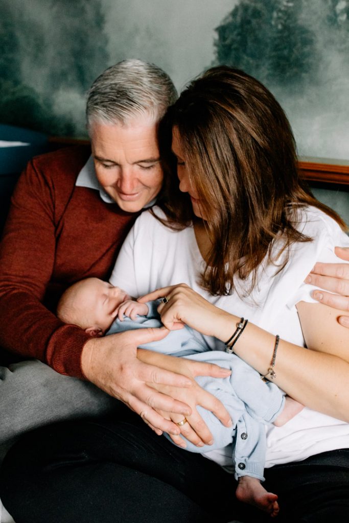 Mum and dad are sitting on the bed and cuddling their newborn baby boy. Newborn photographer in Hampshire. Ewa Jones Photography