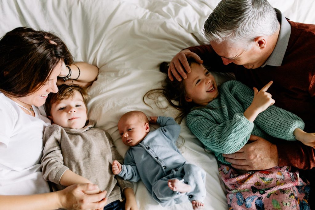 family of 5 is all laying on bed and interacting with each other. Natural unposed newborn photo shoot at home. Basingstoke, hampshire. Ewa Jones Photography