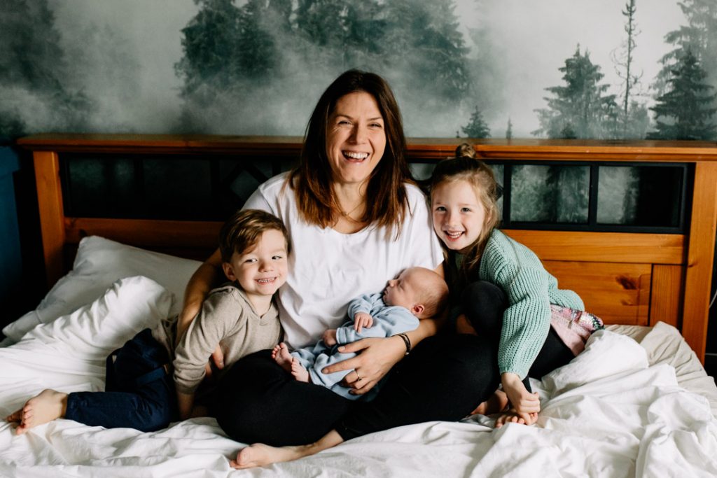 Mum and her children are on bed and they are all smiling. Newborn baby photo shoot in Hampshire. Ewa Jones Photography
