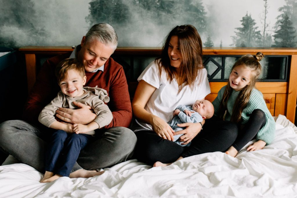 family is sitting on bed and all smiling. Newborn natural unposed family photo shoot in Basingstoke, Hampshire. Ewa Jones Photography