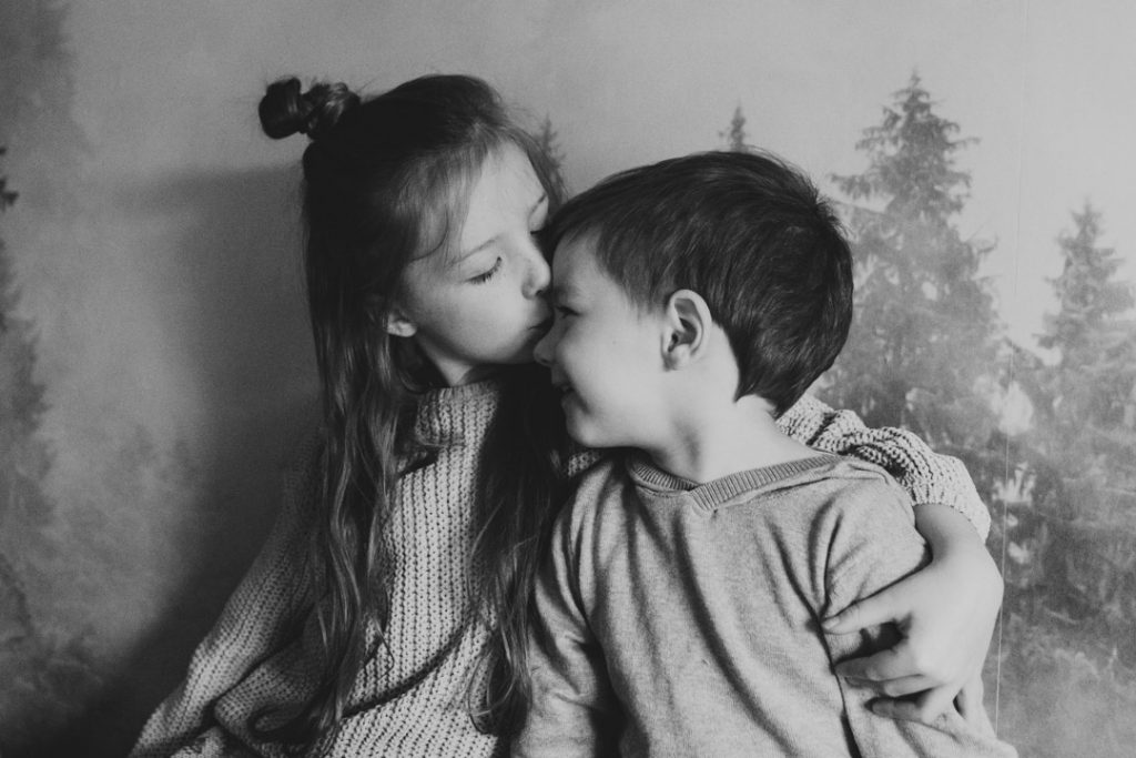 Brother and sister are cuddling up to each other and older sister is kissing her brother on this nose. family photo shoot in Hampshire. Ewa Jones Photography