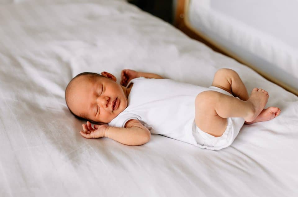 Newborn photoshoot in Hampshire. Newborn baby is sleeping on the bed and wearing white baby grow. How to edit your photos like a Pro. Ewa Jones Photography