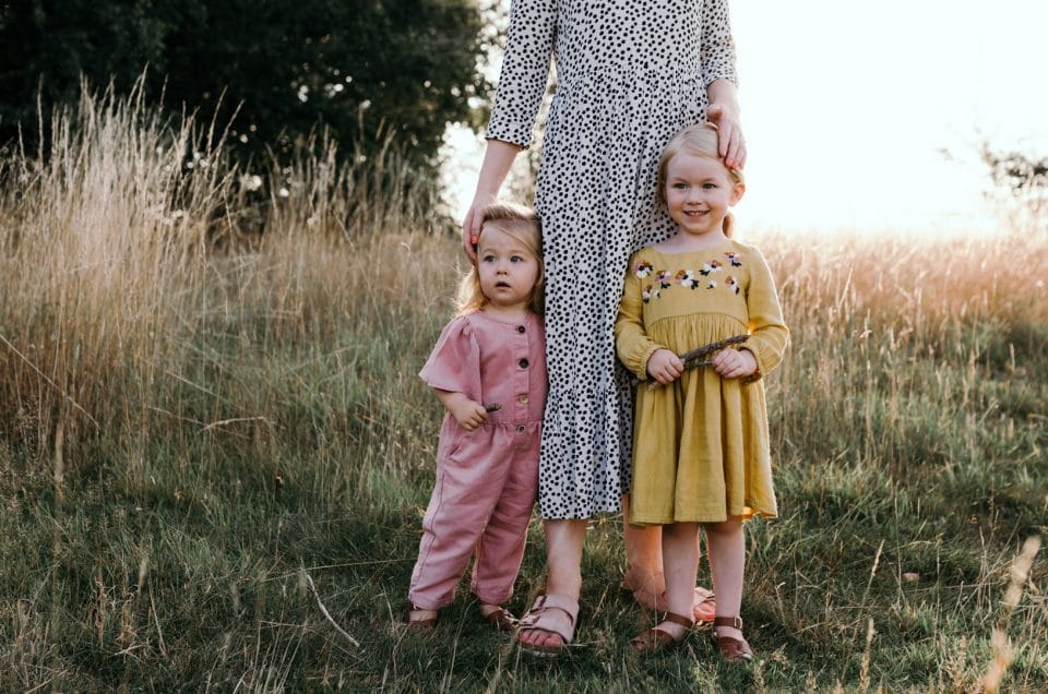 Two girls are standing in the fields of wild grass. Family photographer in Hampshire. Ewa Jones Photography. Before and after examples of my work.