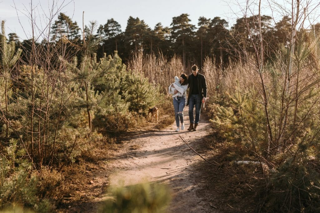 family of three is walking in the lovely common. Mum is holding baby boy. Winter family photo shoot. Hampshire photographer. Ewa Jones Photography