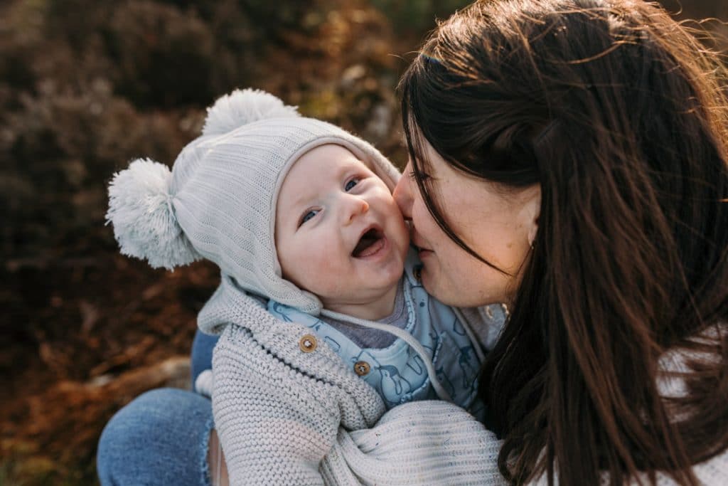 little baby boy is laughing and mum is trying to kiss him. Outdoor family photo shoot in Hampshire. Ewa Jones Photography