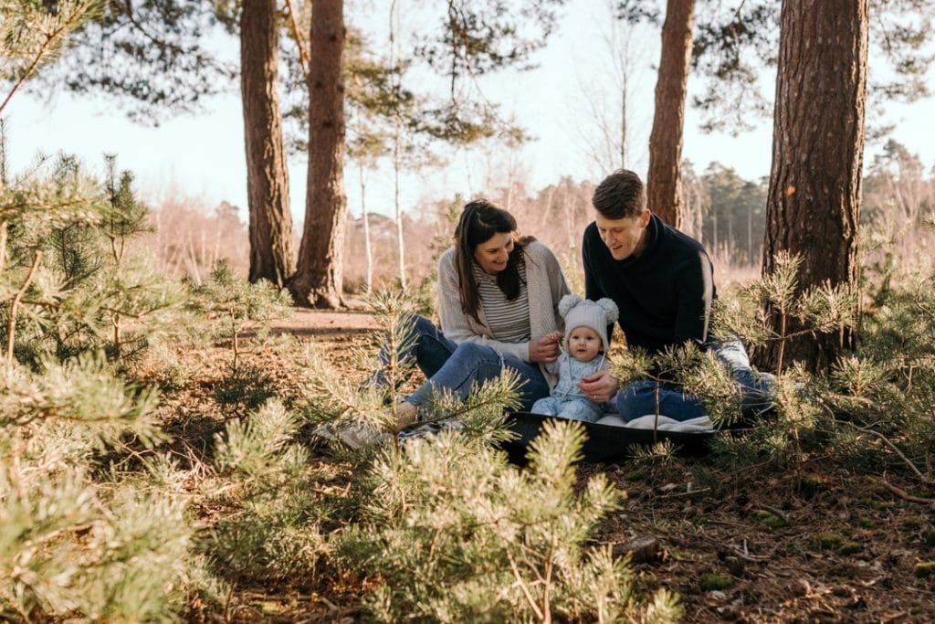 Family is sitting on the blanket and mum and dad are looking at their baby boy. Lovely natural lifestyle family photography. Outdoor family photo session in the winter. Ewa Jones Photography