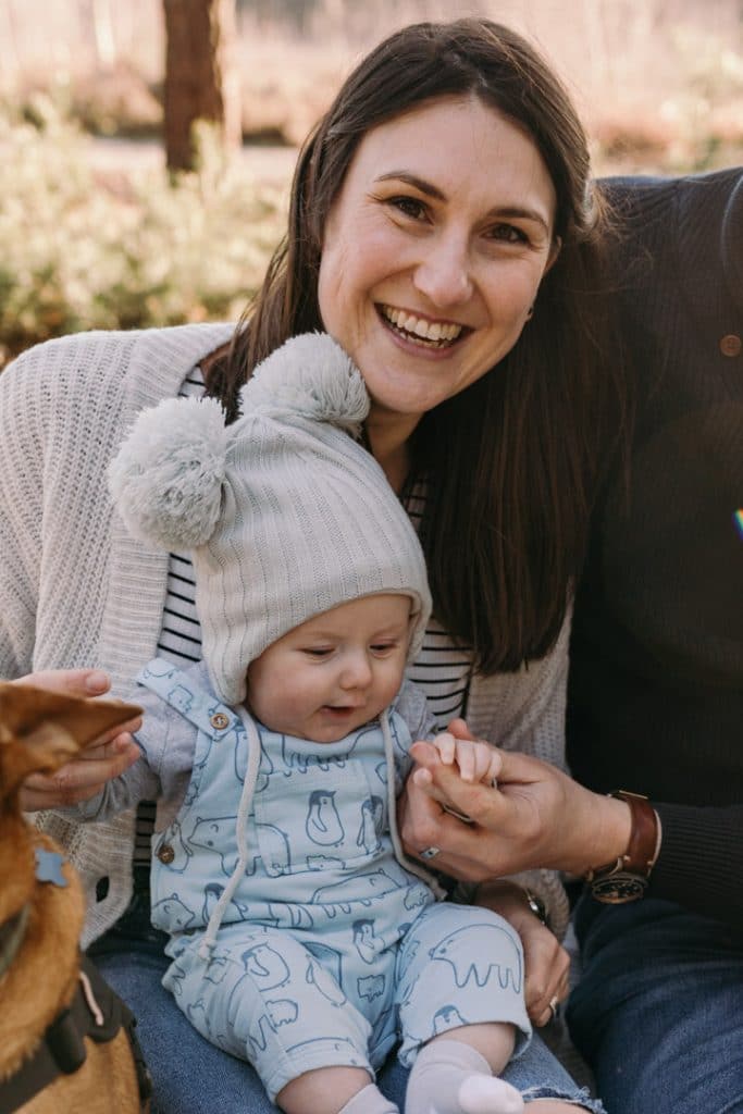 Mum is looking at the camera and laughing. she is holding baby boy in her arms. Family photographer in Hampshire. Ewa Jones Photography