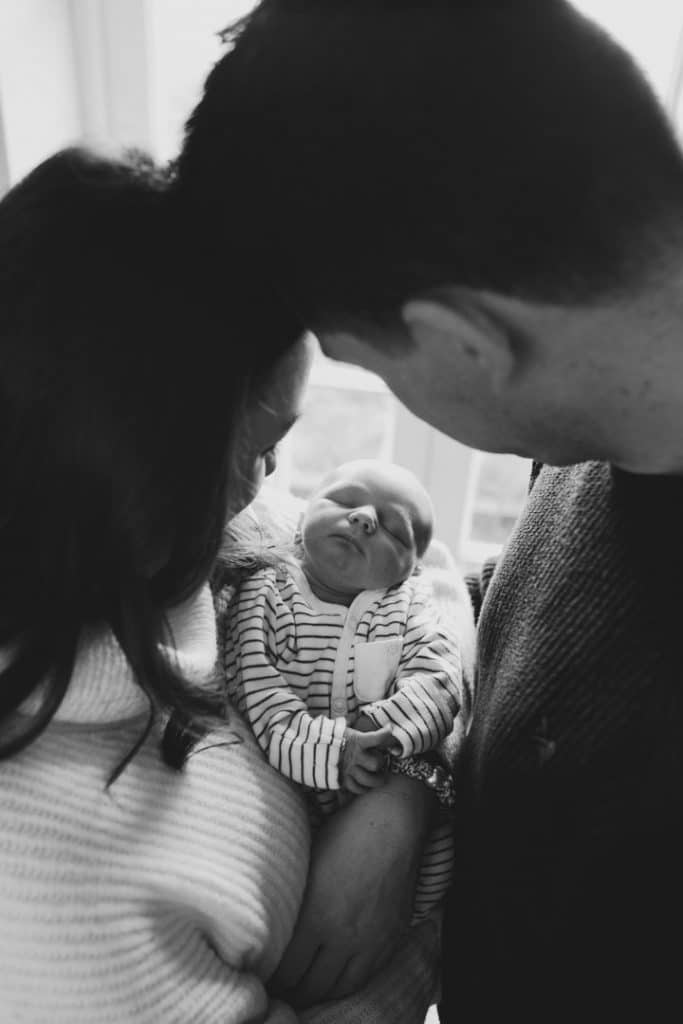 Mum and dad are holding newborn baby and looking down on him. Newborn photoshoot in Hampshire. Ewa Jones Photography