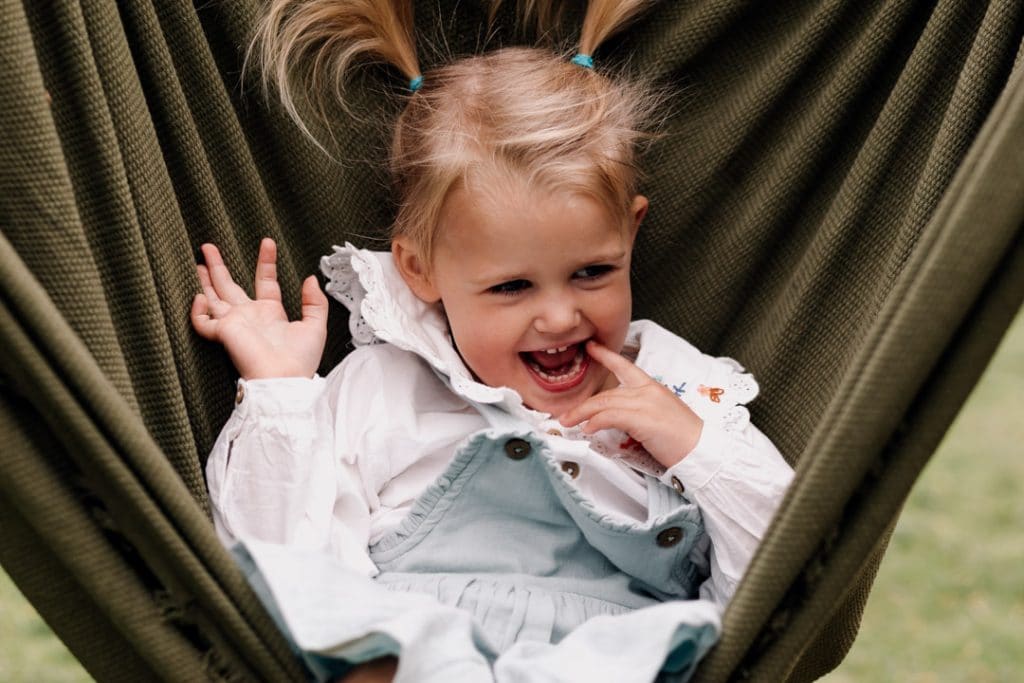 Little girl is sitting in the blanket and parents are swaying her. Benefits of an outdoor family photoshoot. Basingstoke photographer. Ewa Jones Photography.