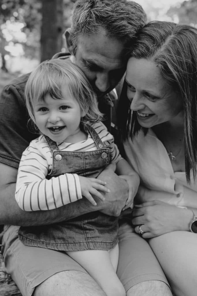 Mum and dad are cuddling their girl and she is smiling. Lifestyle family photographer in Hampshire. Hampshire photographer. Ewa Jones Photography