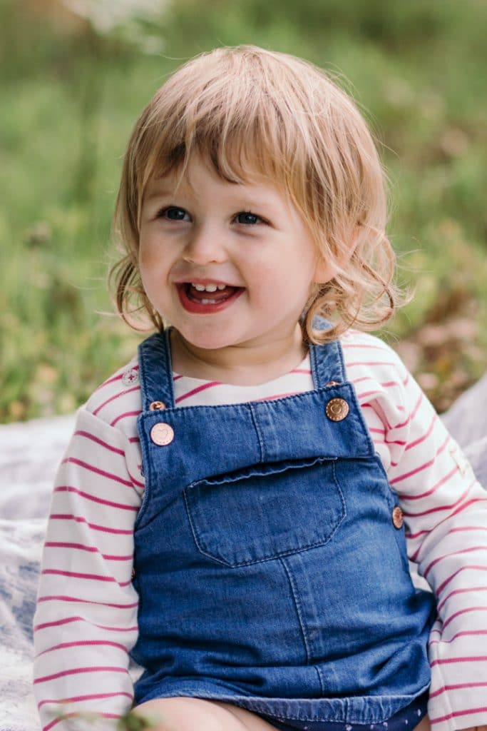What to wear for a family photo session. Little girl is sitting on the blanket and smiling. Hampshire photographer. Ewa Jones Photography