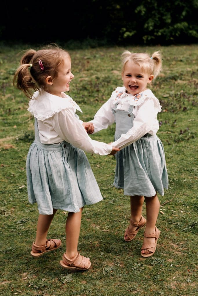 Two sisters are laughing and jumping on the grass. Family photography in Basingstoke. Basingstoke photographer. Ewa Jones Photography