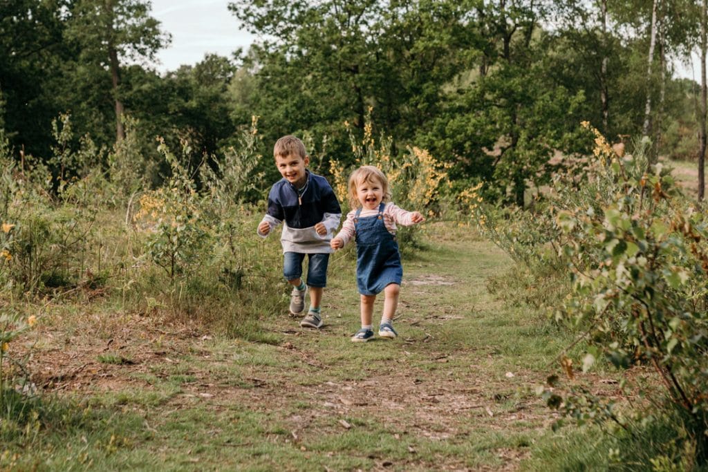 Sister and brother are running on the field. natural outdoor family photo session in Hampshire. Ewa Jones Photography