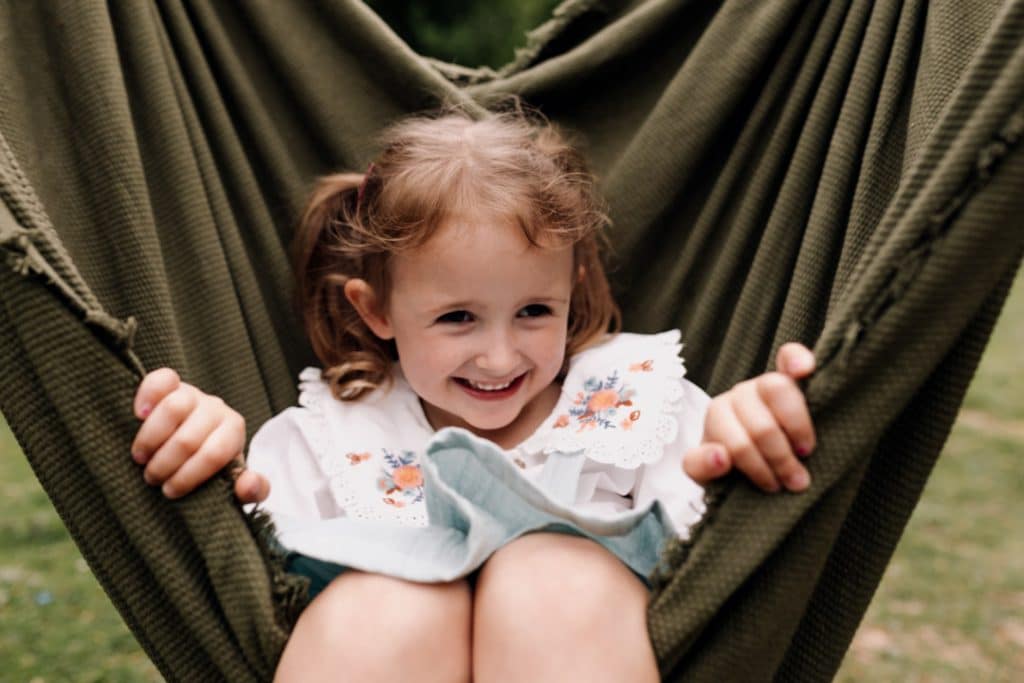 Little girl is sitting in the blanket and parents are swaying her. Benefits of an outdoor family photoshoot. Basingstoke photographer. Ewa Jones Photography.