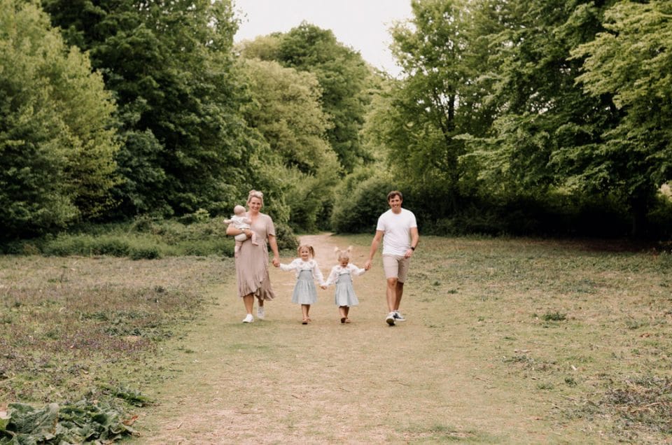 Family is walking on the field towards the photographer. Natural lifestyle family photo session. Ewa Jones Photography