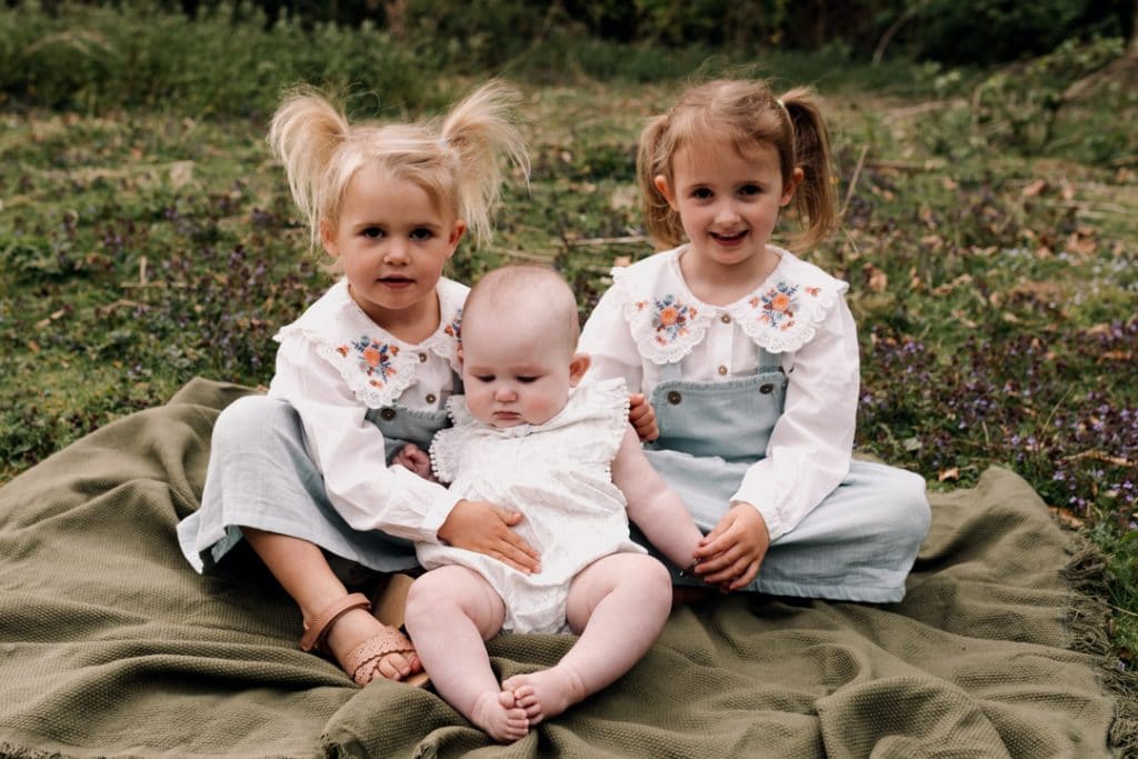 Three sisters are sitting on the blanket and holding hands. Hampshire photographer. Ewa Jones Photography