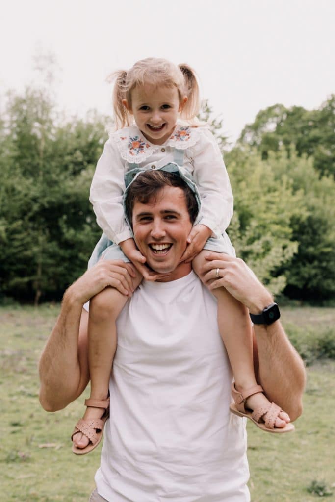 Dad is holding his girl on the shoulders and they are both smiling to the camera. Family photographer in Basingstoke, Hampshire. Ewa Jones Photography