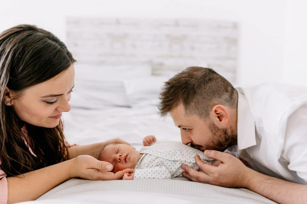 mum and dad are looking at their newborn baby boy. Dad is kissing boy on his tummy. Newborn photographer in Basingstoke, Ewa Jones Photography