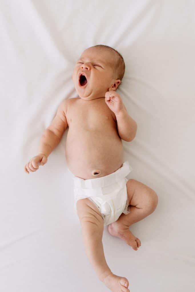 Newborn baby is laying on the bed in the nappy and yawning. Newborn photographer in Basingstoke, Hampshire. Ewa Jones Photography
