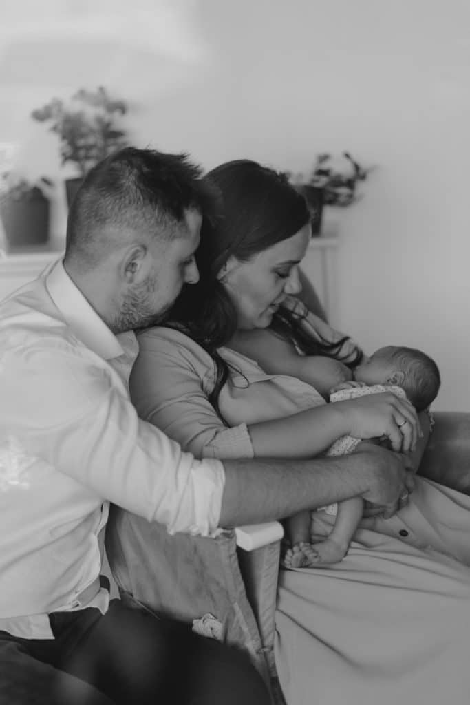 Black and white image of newborn parents sitting and mum is breastfeeding. Basingstoke photographer. Ewa Jones Photography