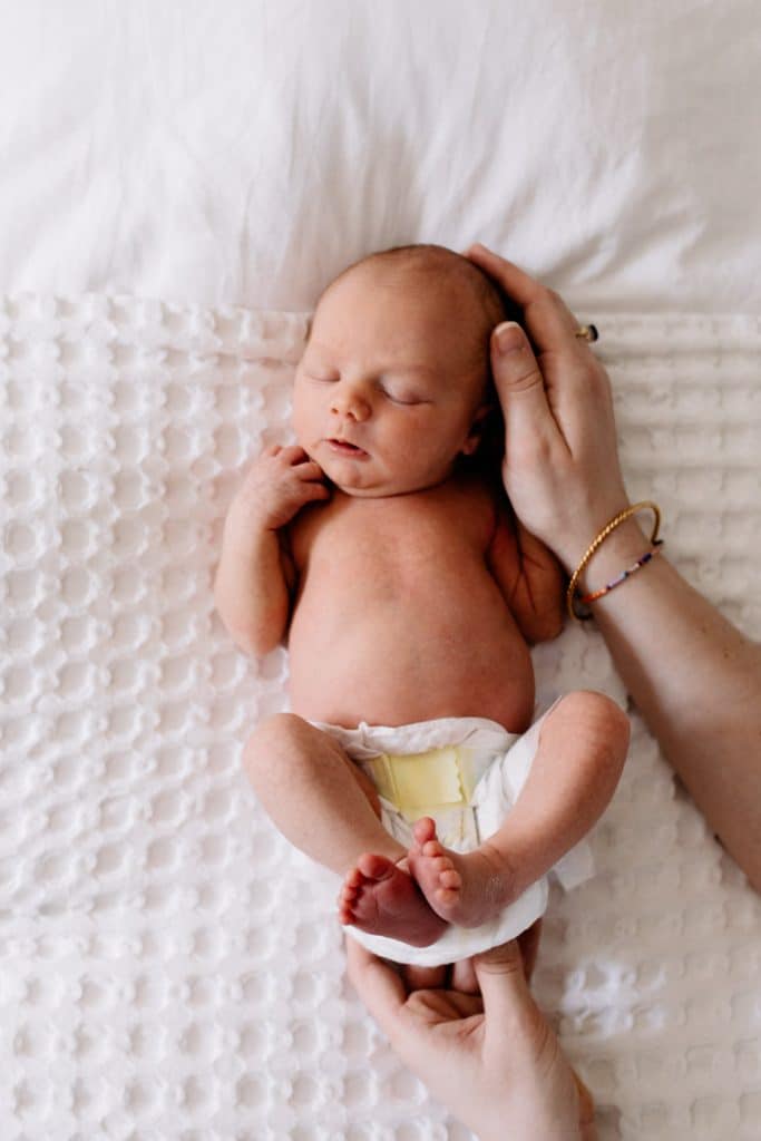 newborn on the bed in his nappy and mum is holding newborn baby head. Newborn photographer in Hampshire. Ewa Jones Photography