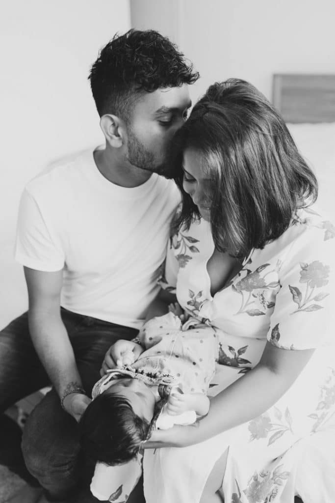 Parents are sitting on the edge of bed and cuddling. Newborn photo session in London. Ewa Jones Photography