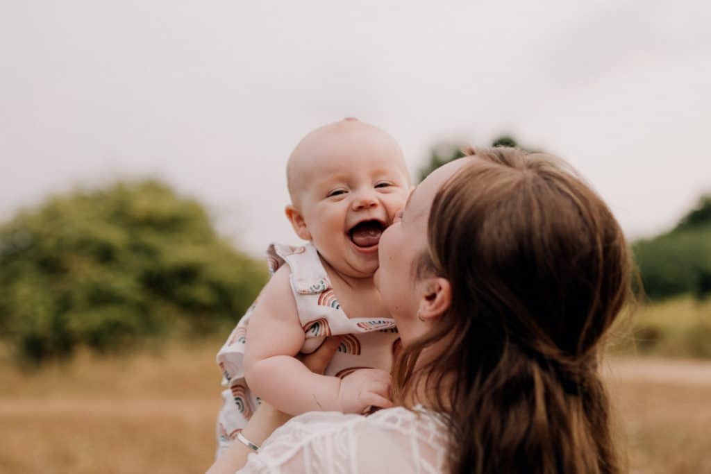 Mum is cuddling her baby girl and holding up. her baby girl is looking at the camera and smiling. Natural lifestyle photo session in Hampshire. Hampshire photographer. Ewa Jones Photography