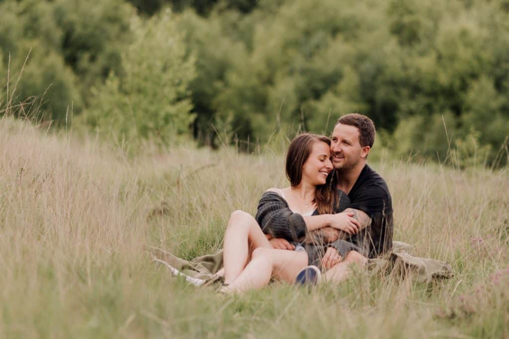 couple is sitting on the grass and cuddling to each other. they are smiling. Engagement photo session in Basingstoke. Ewa Jones Photography