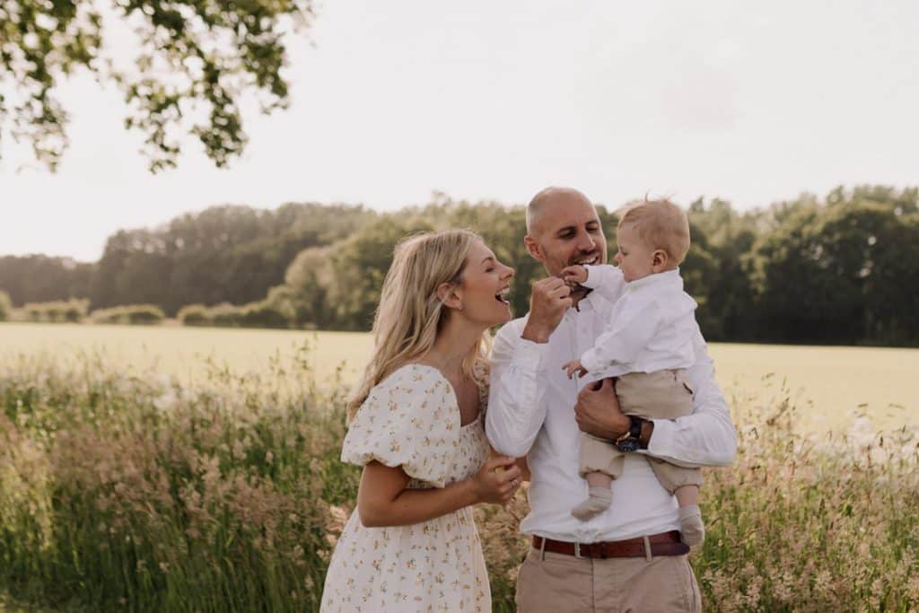 Family photo session in Hampshire countryside-1 Mum and dad are looking at their boy and smiling to him. They are all wearing lovely white and cream outfits. Family photo session in Hampshire. Family photographer in Hampshire. Ewa Jones Photography