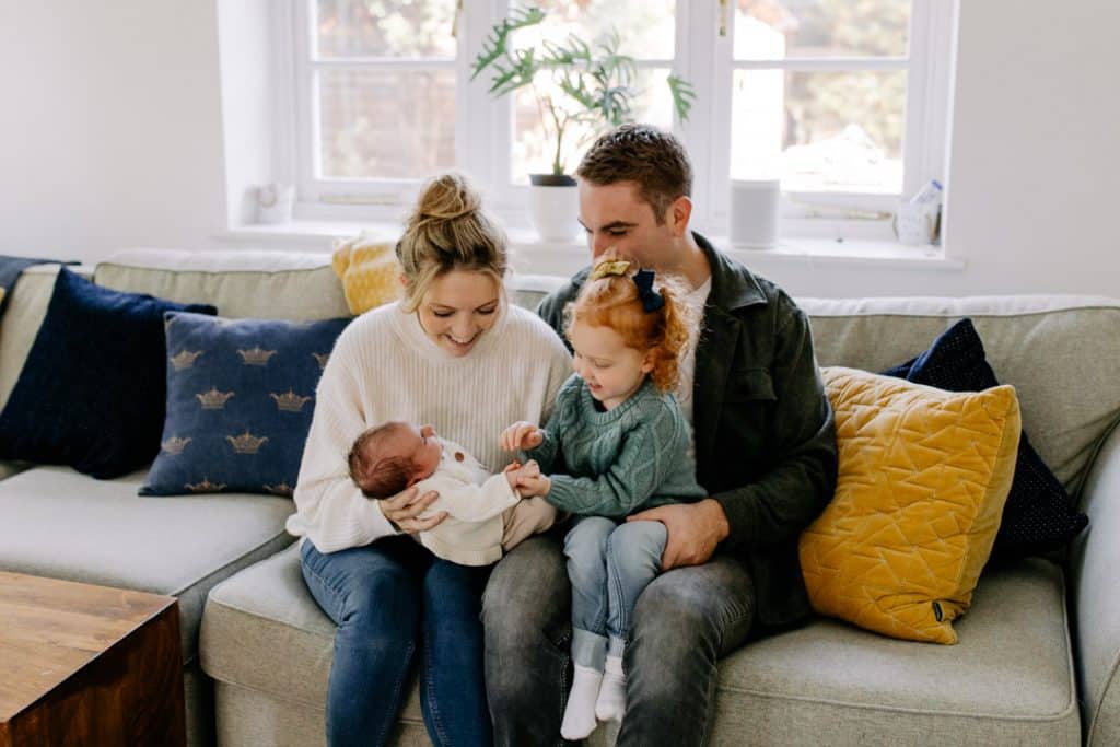 family of four is on the sofa. mum dad and older sister are looking at their baby. Newborn photographer in Hampshire. Ewa Jones Photography