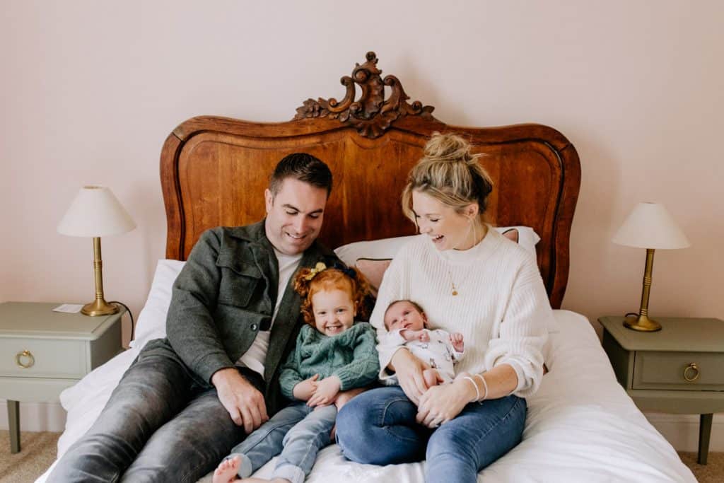 family of four are sitting on the bed an laughing. Newborn photography in Hampshire. Ewa Jones Photography
